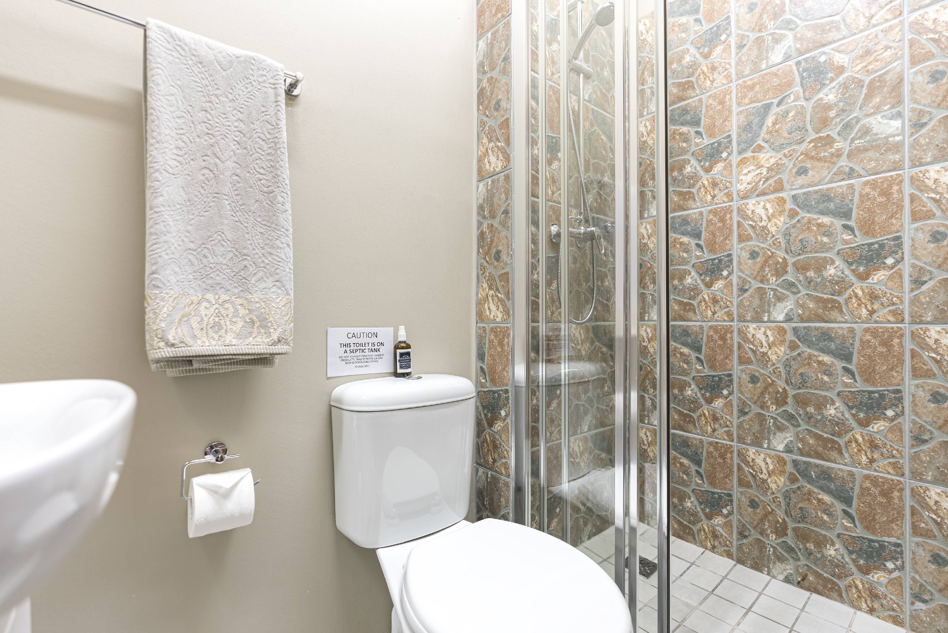 Un baño con inodoro, lavabo y ducha con pared de piedra.