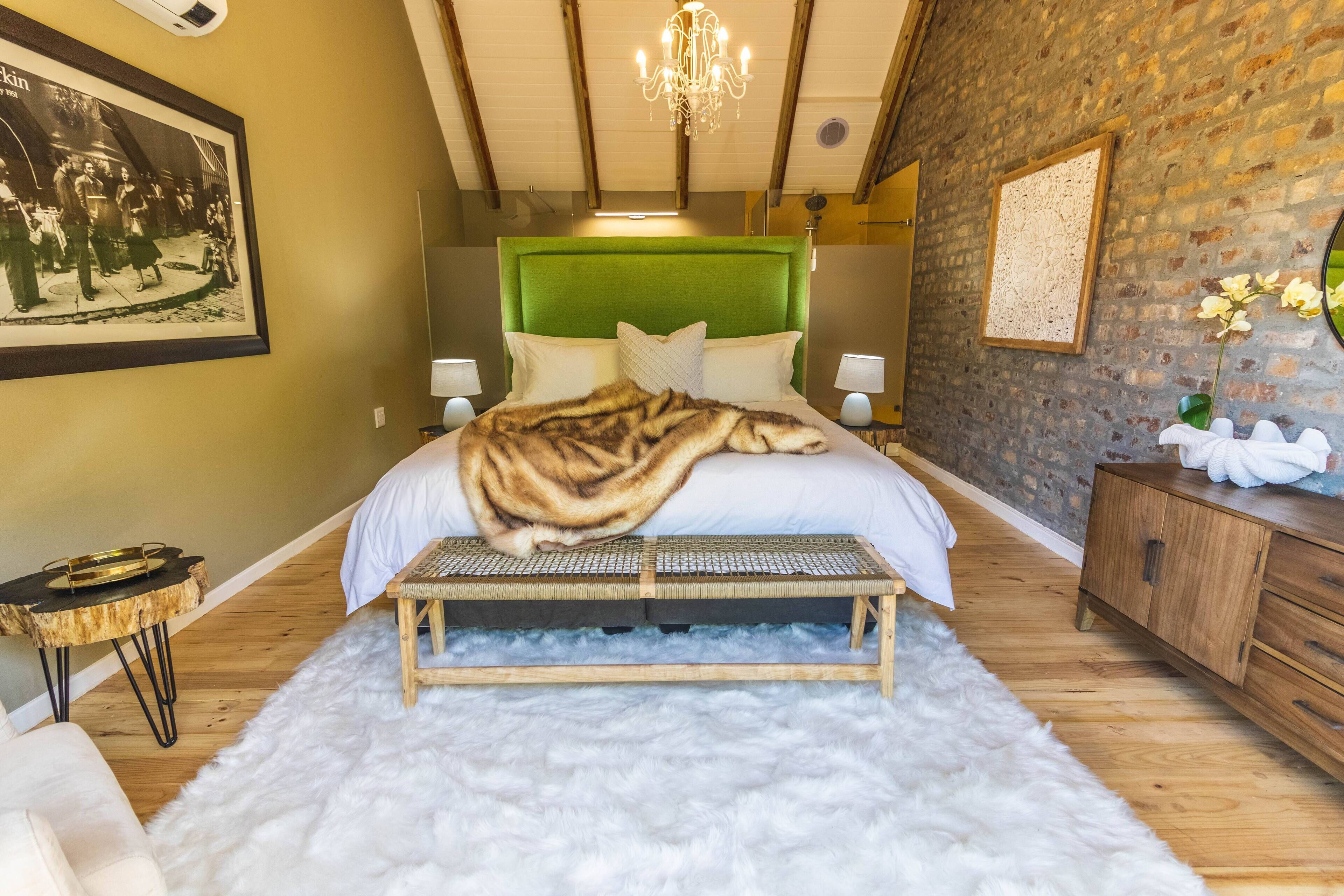 A bedroom with a bed, a bench, a dresser, a chandelier, and a framed picture on the wall.
