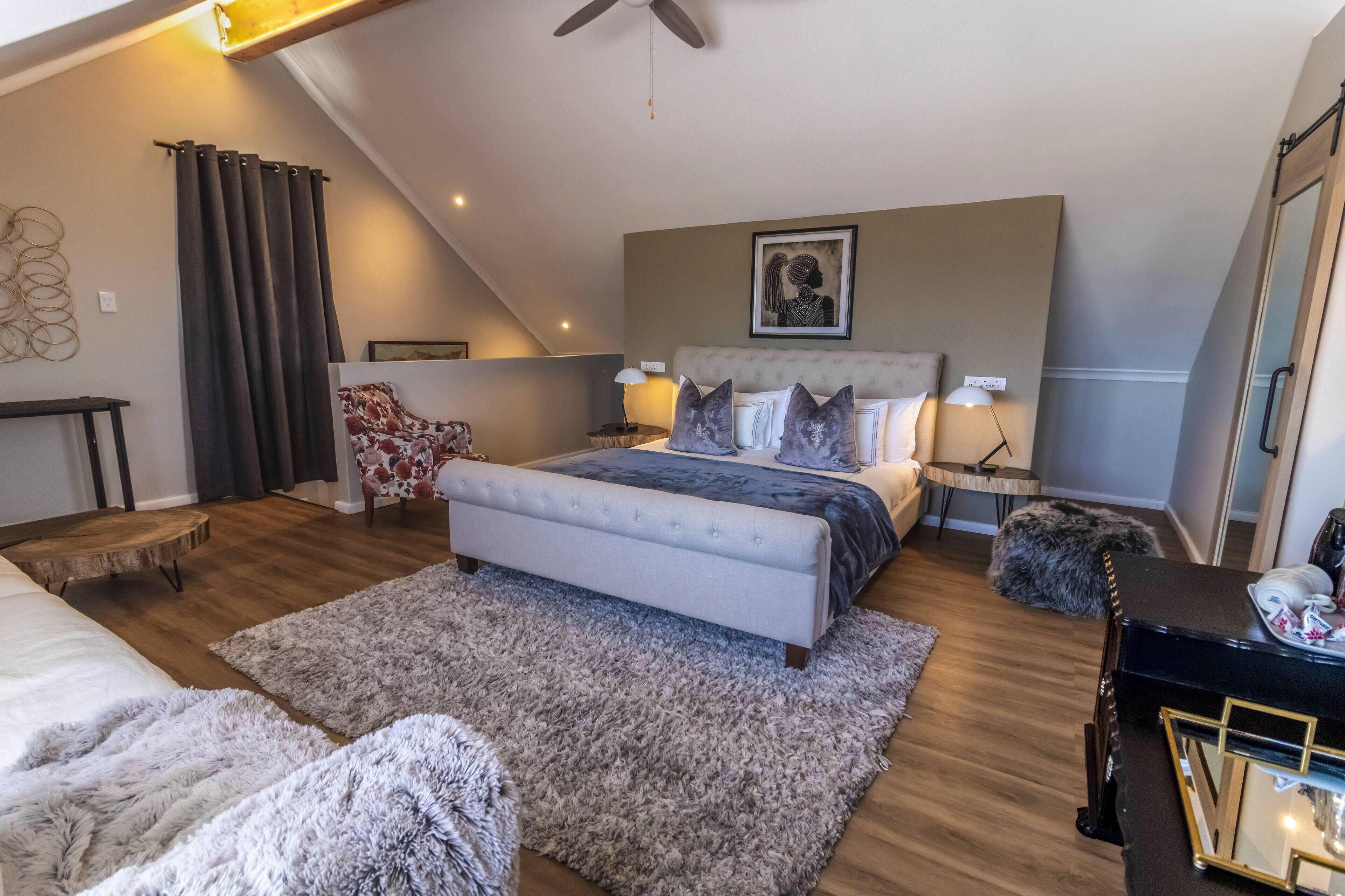 Ein Schlafzimmer mit einem Bett, einem Sessel, einem kleinen Tisch, einem Spiegel und einem Deckenventilator.