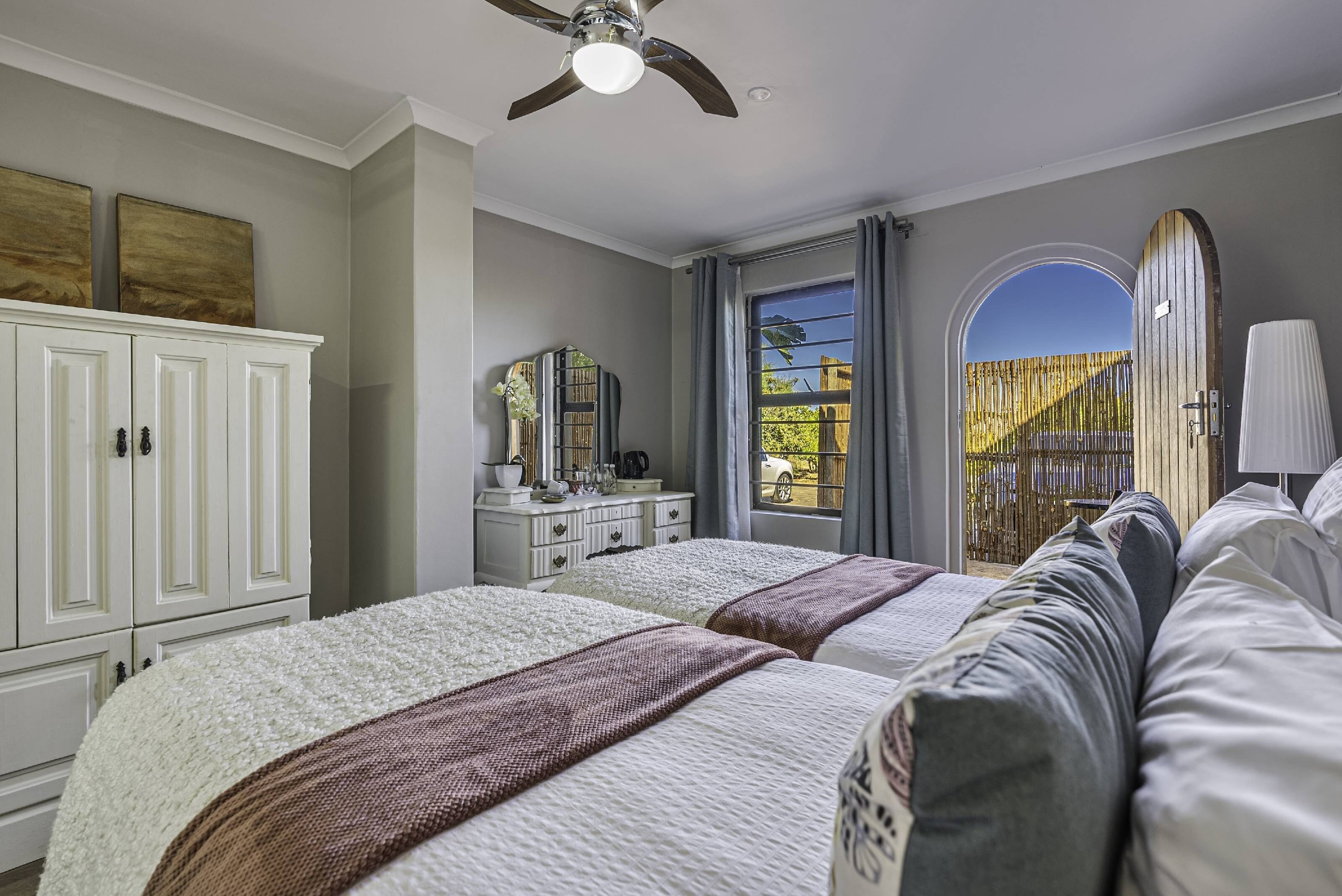 A bedroom with two beds, a ceiling fan, a dresser, and a window with a view of the outside.