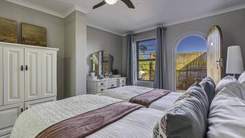 A bedroom with two beds, a ceiling fan, a dresser, and a window with a view of the outside.