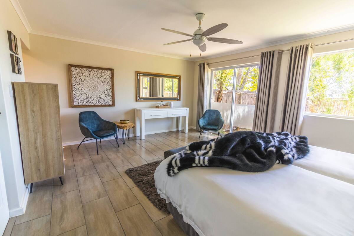 Een slaapkamer met een bed, een bureau, twee stoelen, een plafondventilator en een raam met gordijnen.