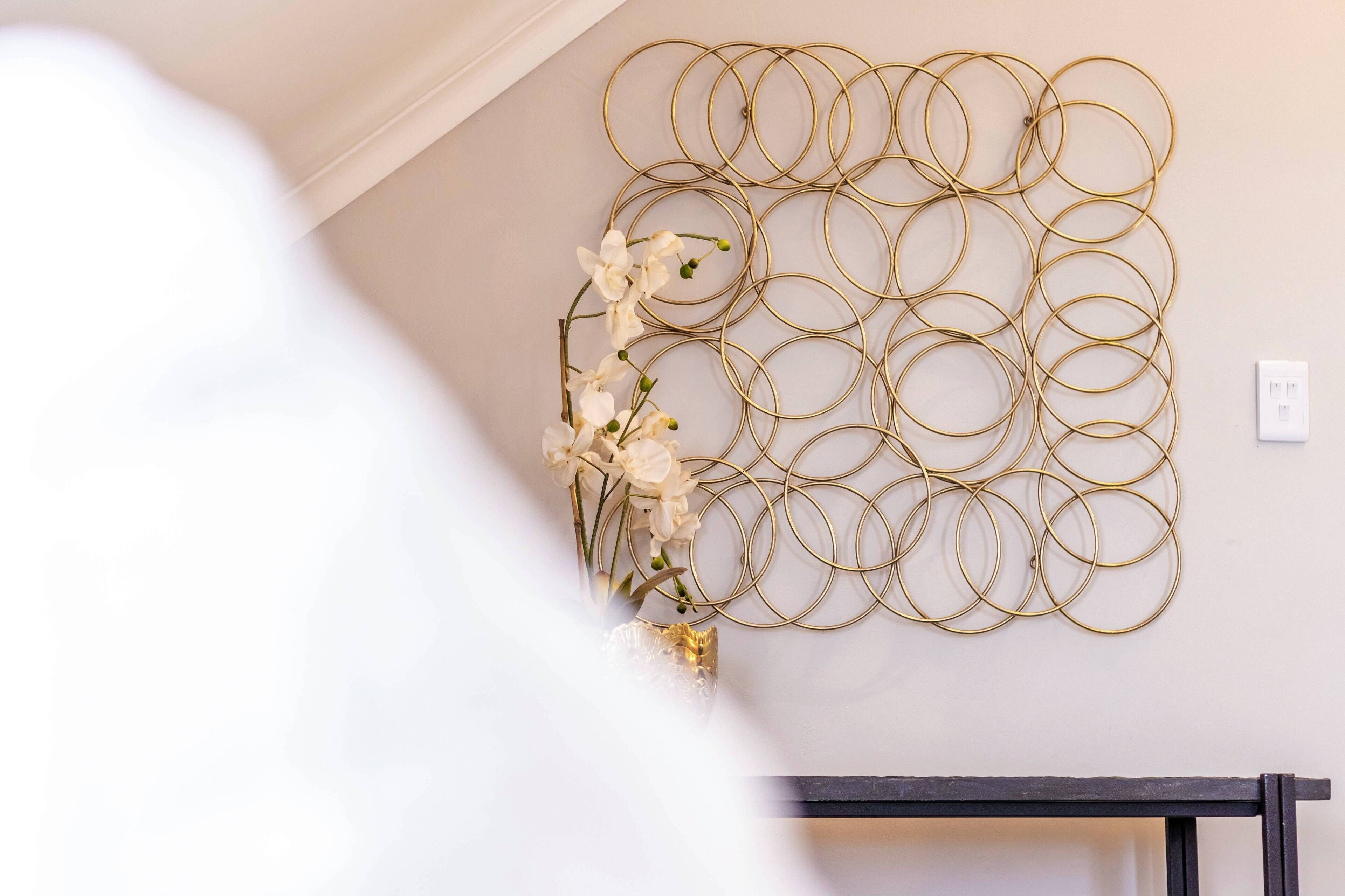 A wall with a gold circular metal art piece and a small white flower arrangement.