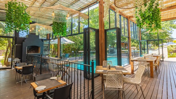 Un espace extérieur aménagé pour les repas, avec des tables et des chaises en bois, un barbecue et une piscine.