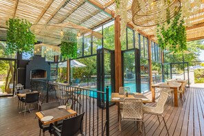 Ein Außenbereich zum Essen mit Holztischen und -stühlen, einem Grill und einem Pool.