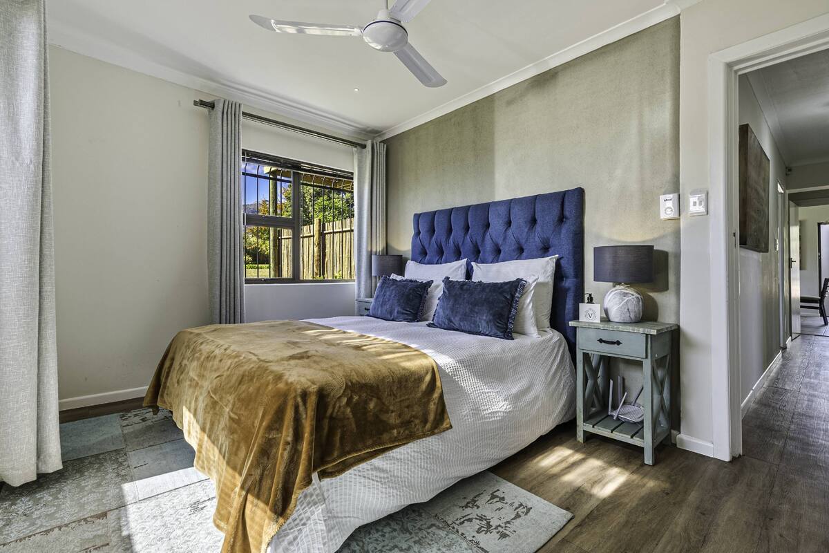 Slaapkamer met een groot bed, een plafondventilator, een nachtkastje met lamp en uitzicht op de natuur door een raam.