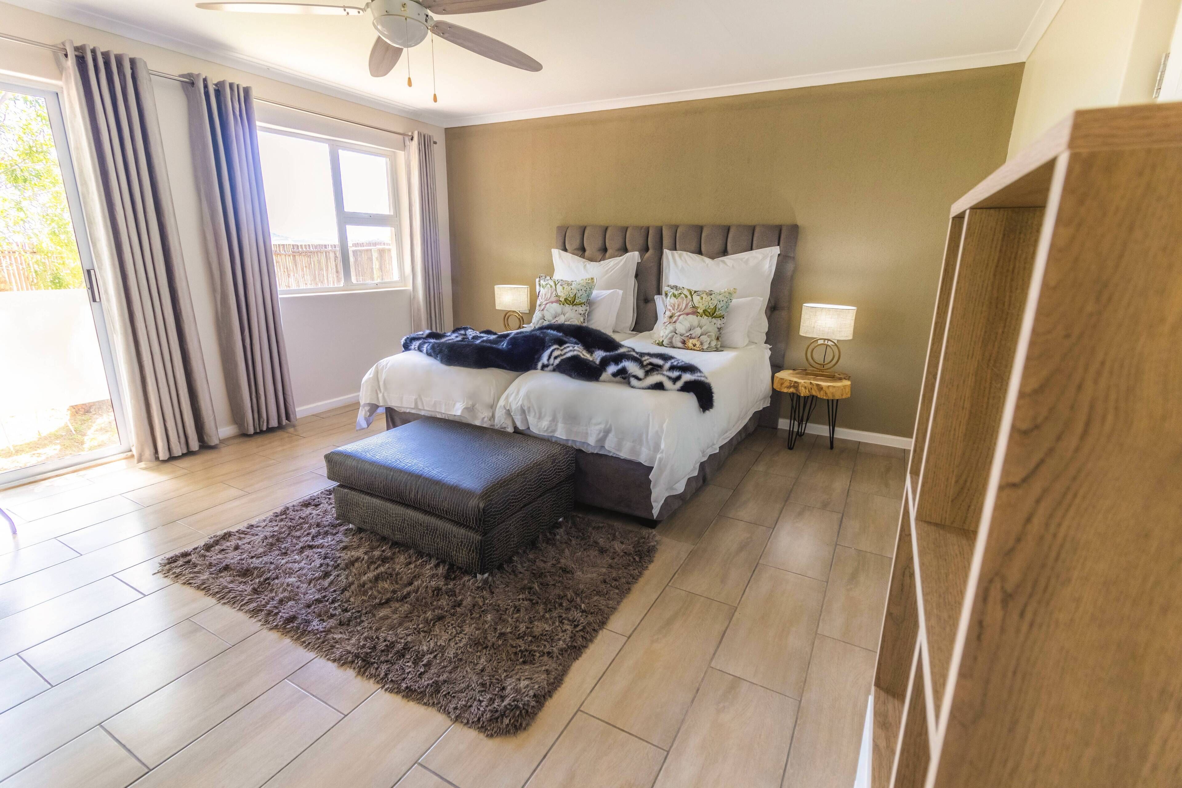 Un dormitorio con cama, mesitas de noche, ventilador de techo y vistas al exterior.