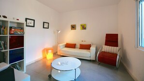 Una sala de estar moderna con un sofá blanco, una mesa redonda de centro, una estantería y una silla roja.