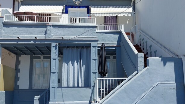 Un edificio de dos pisos con fachada azul, un balcón y una escalera que conduce al piso superior.