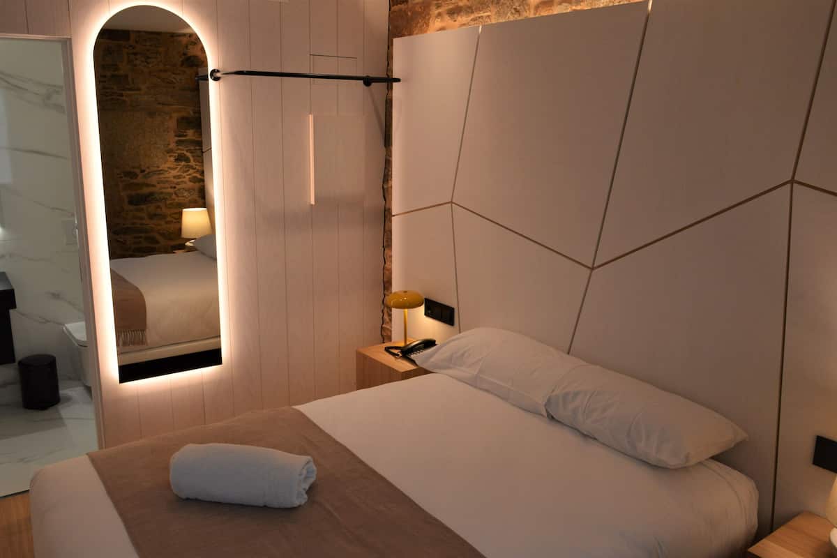 A modern bedroom with a wooden headboard, a bedside lamp, and a neatly made bed with a towel.