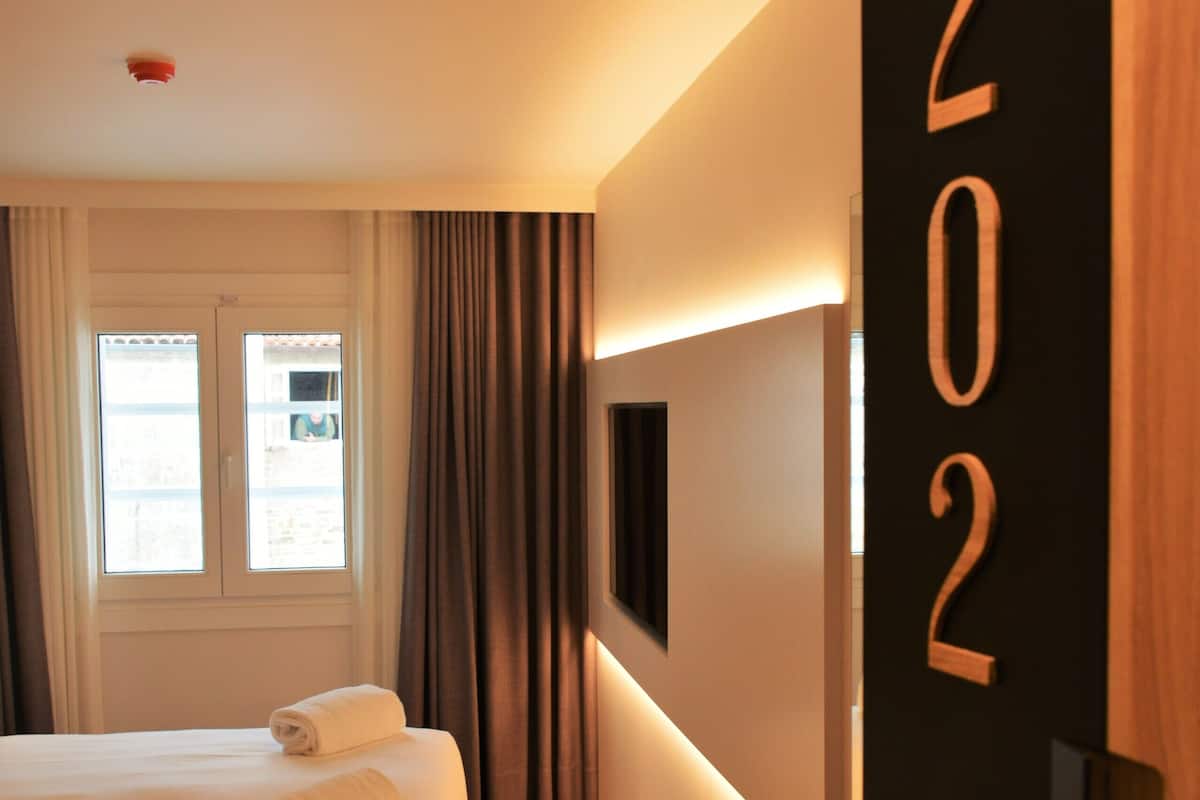 A hotel room with a large bed, a wall-mounted TV, and a number sign indicating room 202.