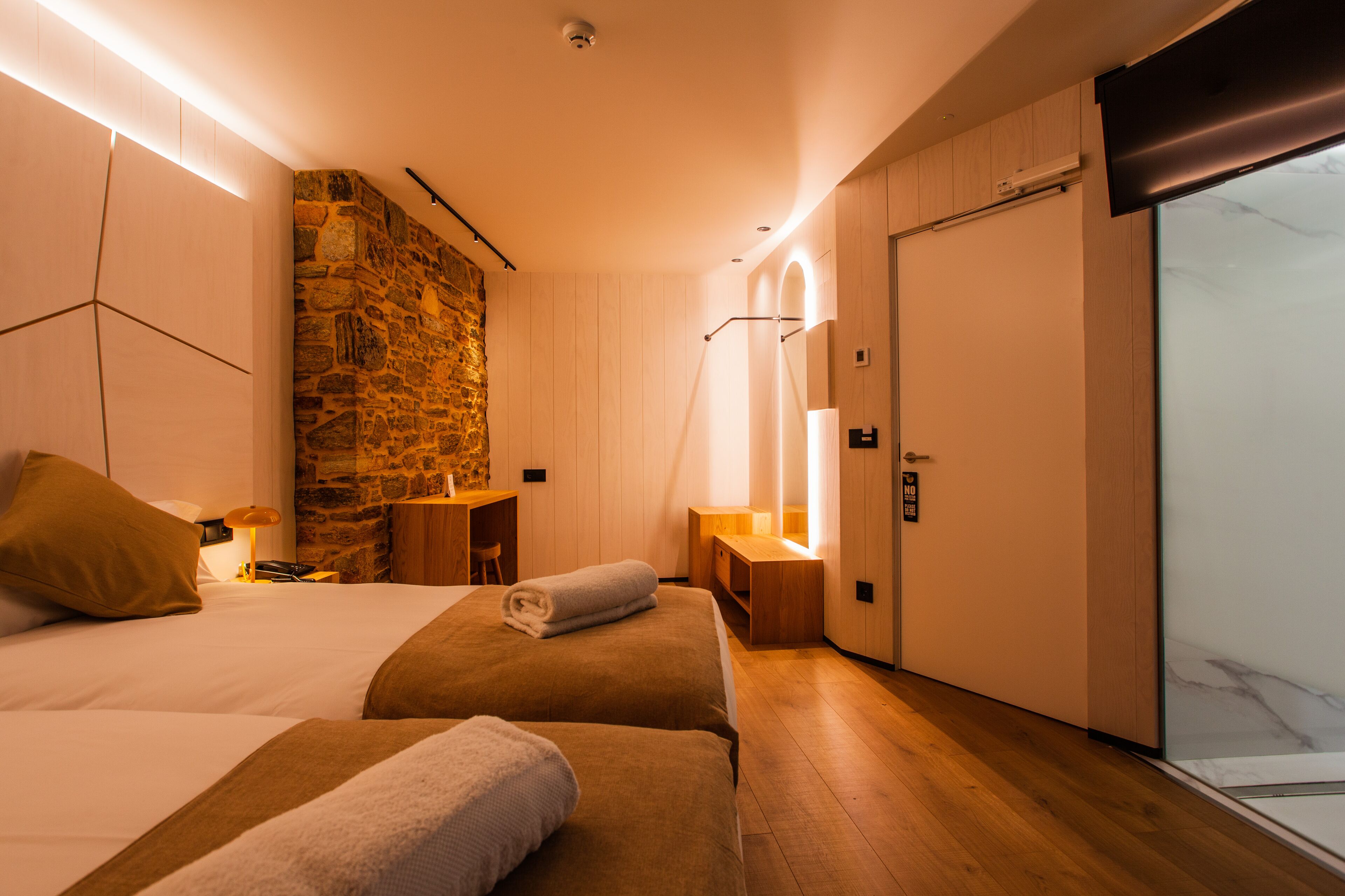 A modern hotel room with two beds, a stone accent wall, a wooden desk, and a large sliding door.