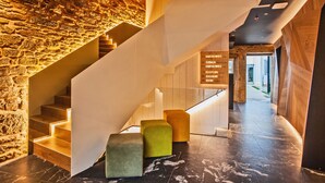 A modern hotel lobby with a stone wall, a wooden staircase, and a reception desk. -  Hotel Plaza Obradoiro by Bossh! Hotels (Santiago de Compostela)