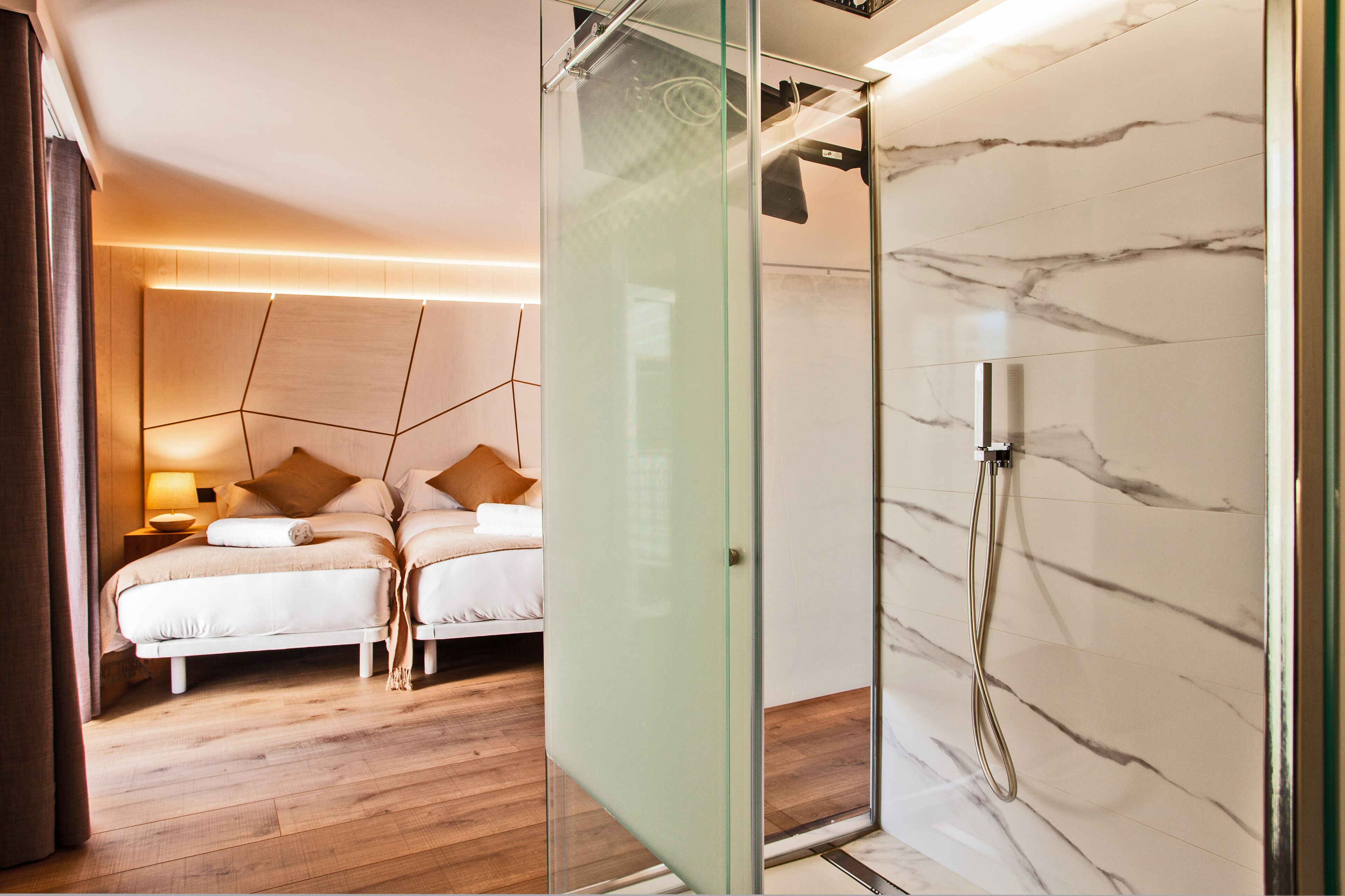 Un dormitorio moderno con separador de vidrio, ducha con paredes de mármol y suelo de madera.