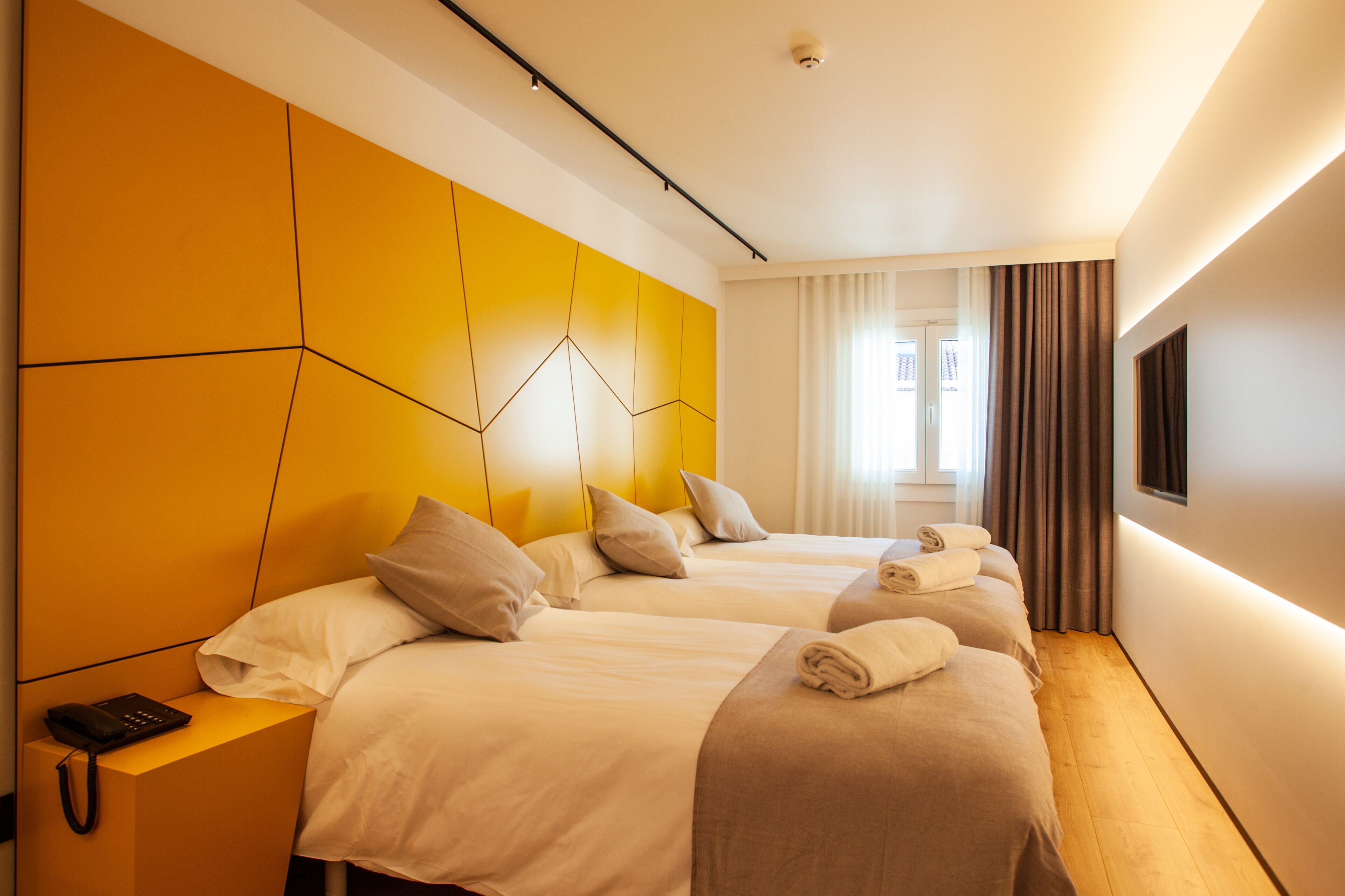 Een hotelkamer met twee bedden, een bedtelefoon en een aan de muur bevestigde televisie.