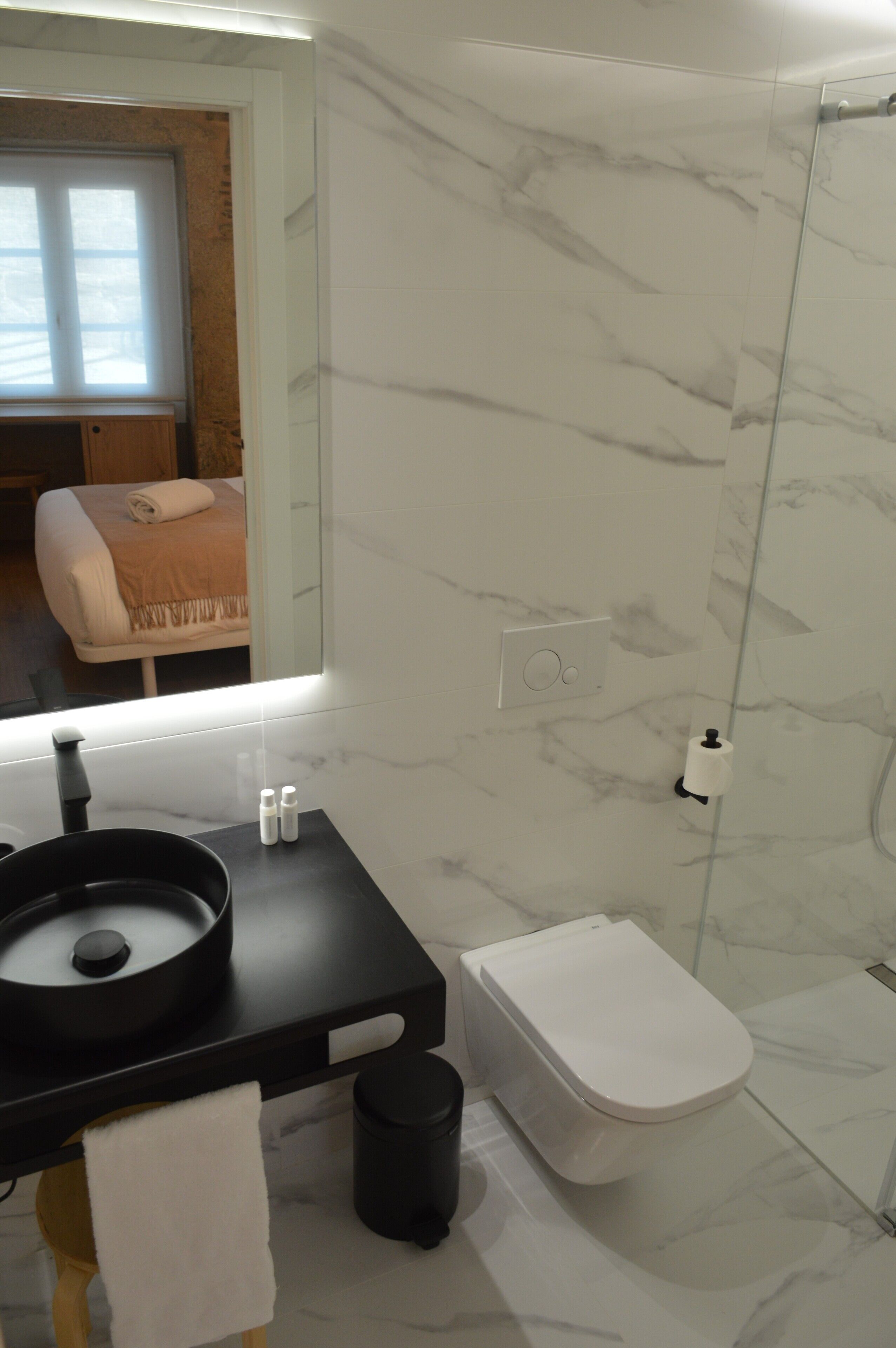 A modern bathroom with a black countertop, white toilet, and marble walls.