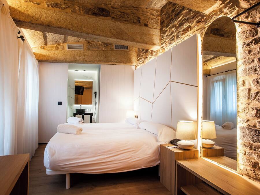 A bedroom with a stone wall, a wooden bed frame, and a nightstand with lamps.