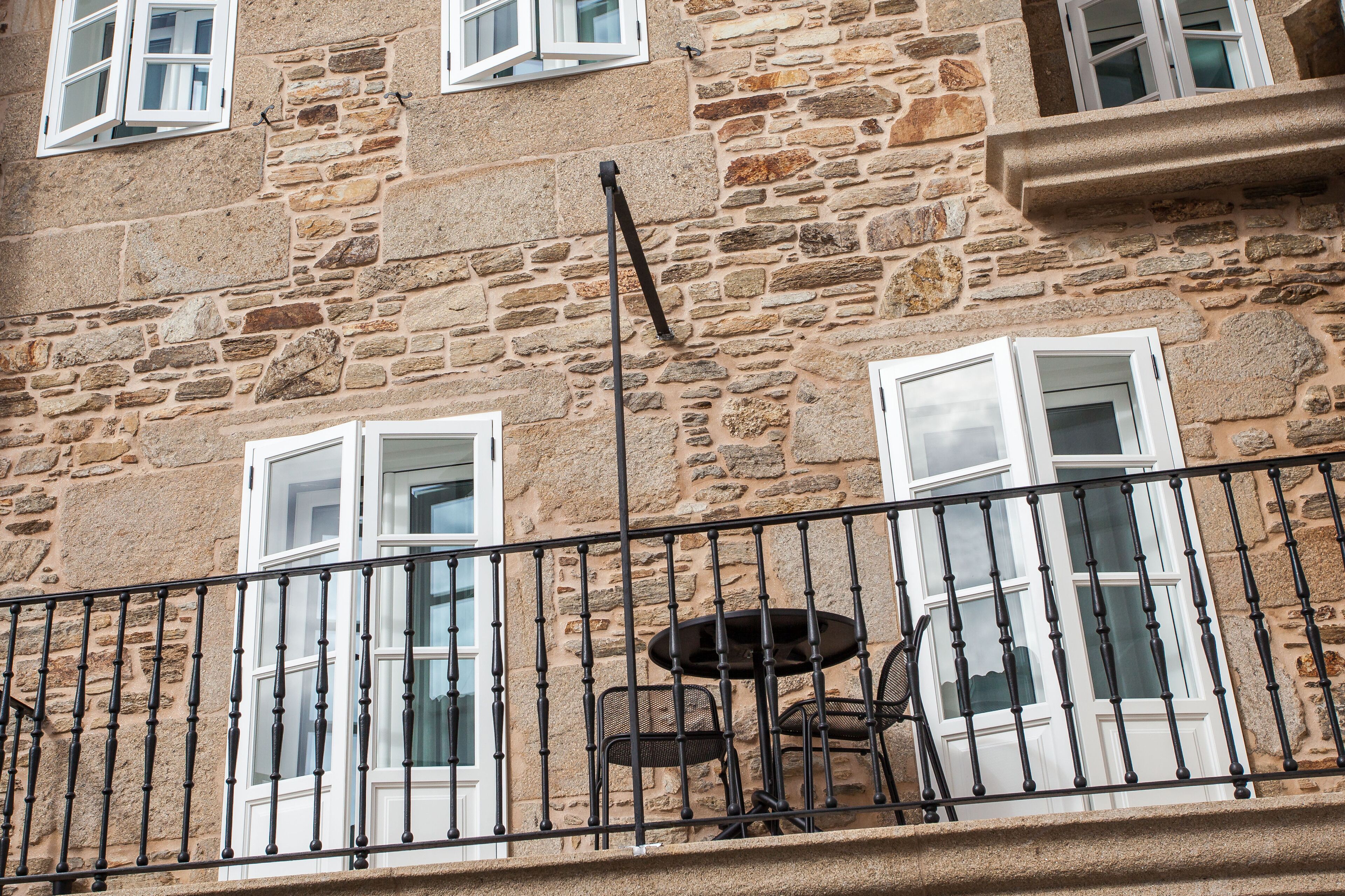 Un bâtiment en pierre doté d’un balcon, de fenêtres à cadre blanc et d’une table entourée de chaises.