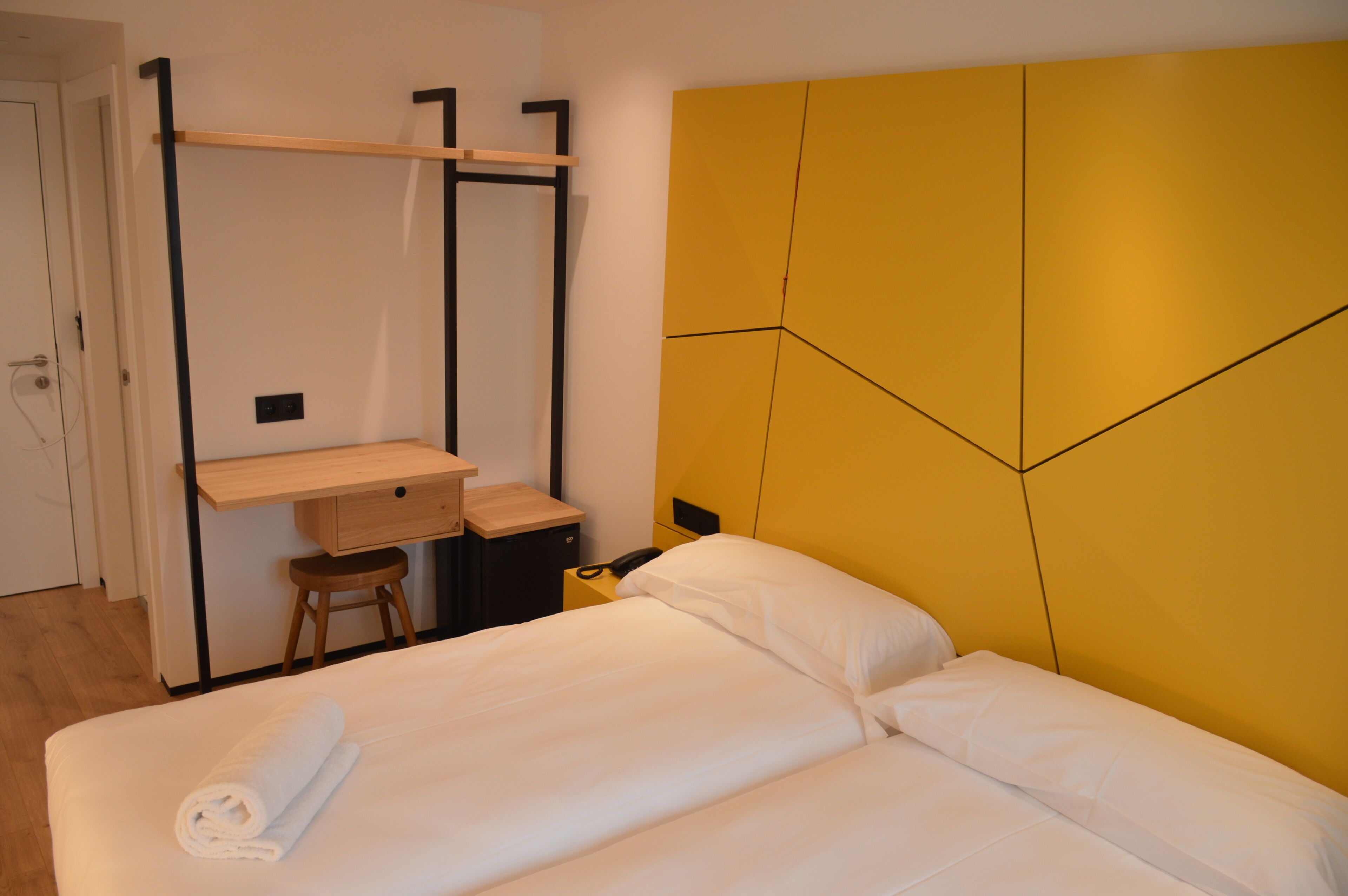 Habitación de hotel con cama, escritorio y silla, y estante en la pared.