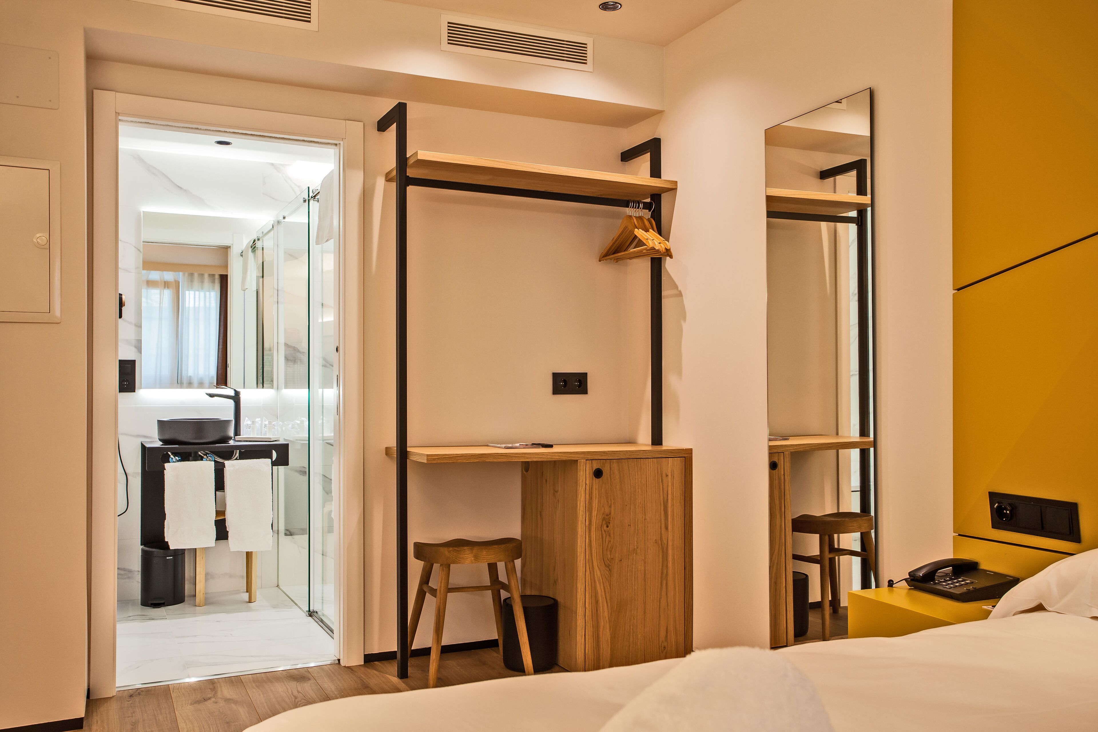 Une chambre d’hôtel de taille réduite, comprenant un lit, un bureau, une chaise, un miroir et une armoire.