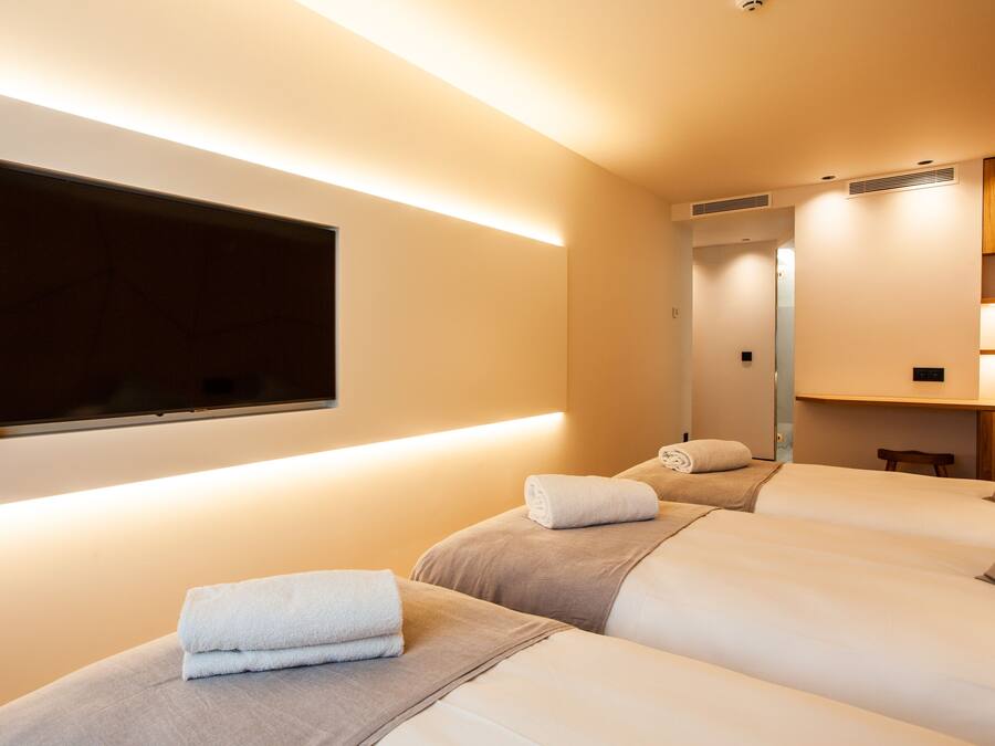 Ein Hotelzimmer mit zwei Betten, einem an der Wand befestigten Flachbildfernseher und einem Spiegel über den Betten.