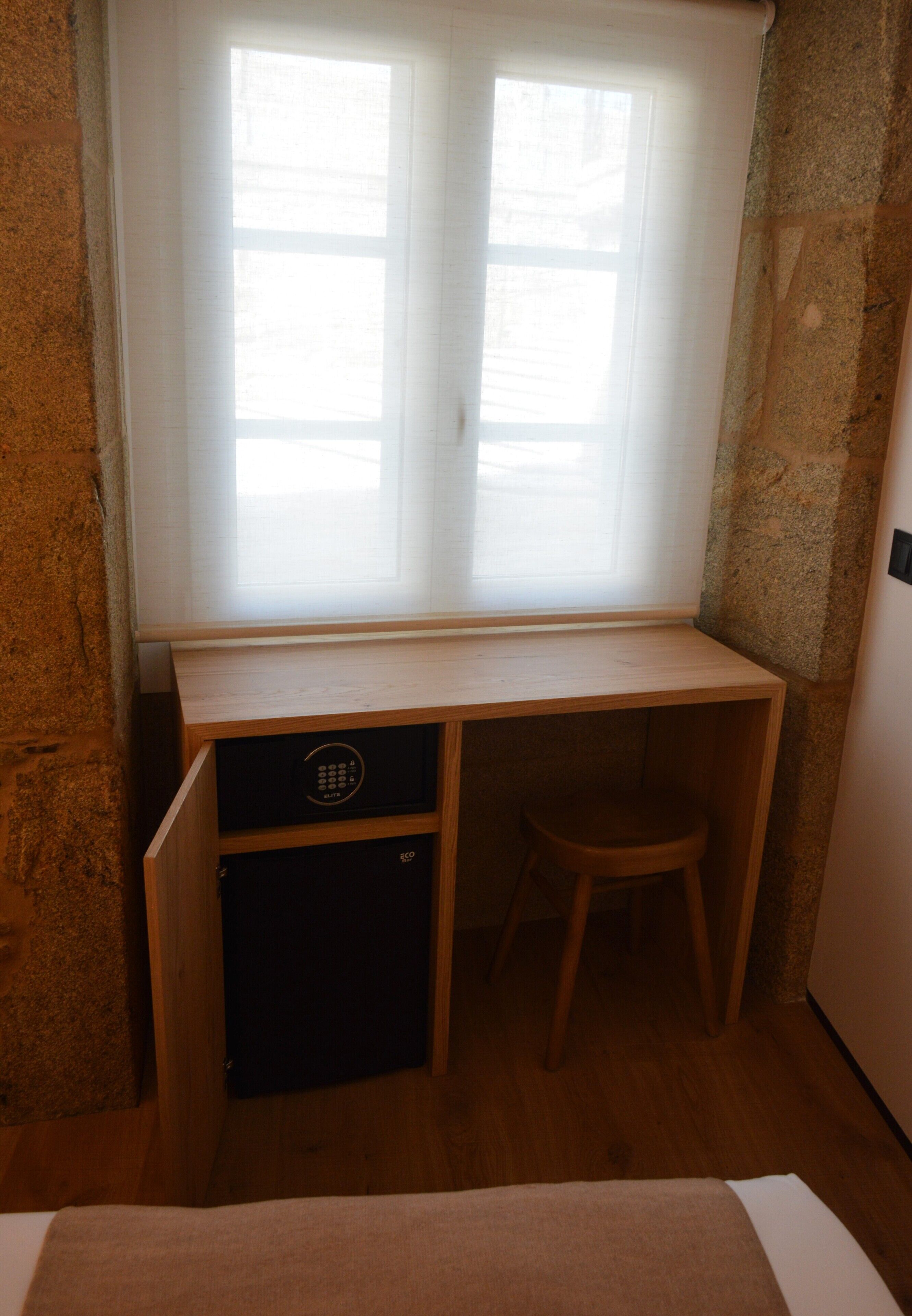 Ein kleiner Holztisch mit Hocker, ein kleines Schränkchen und ein Fenster mit Jalousien.