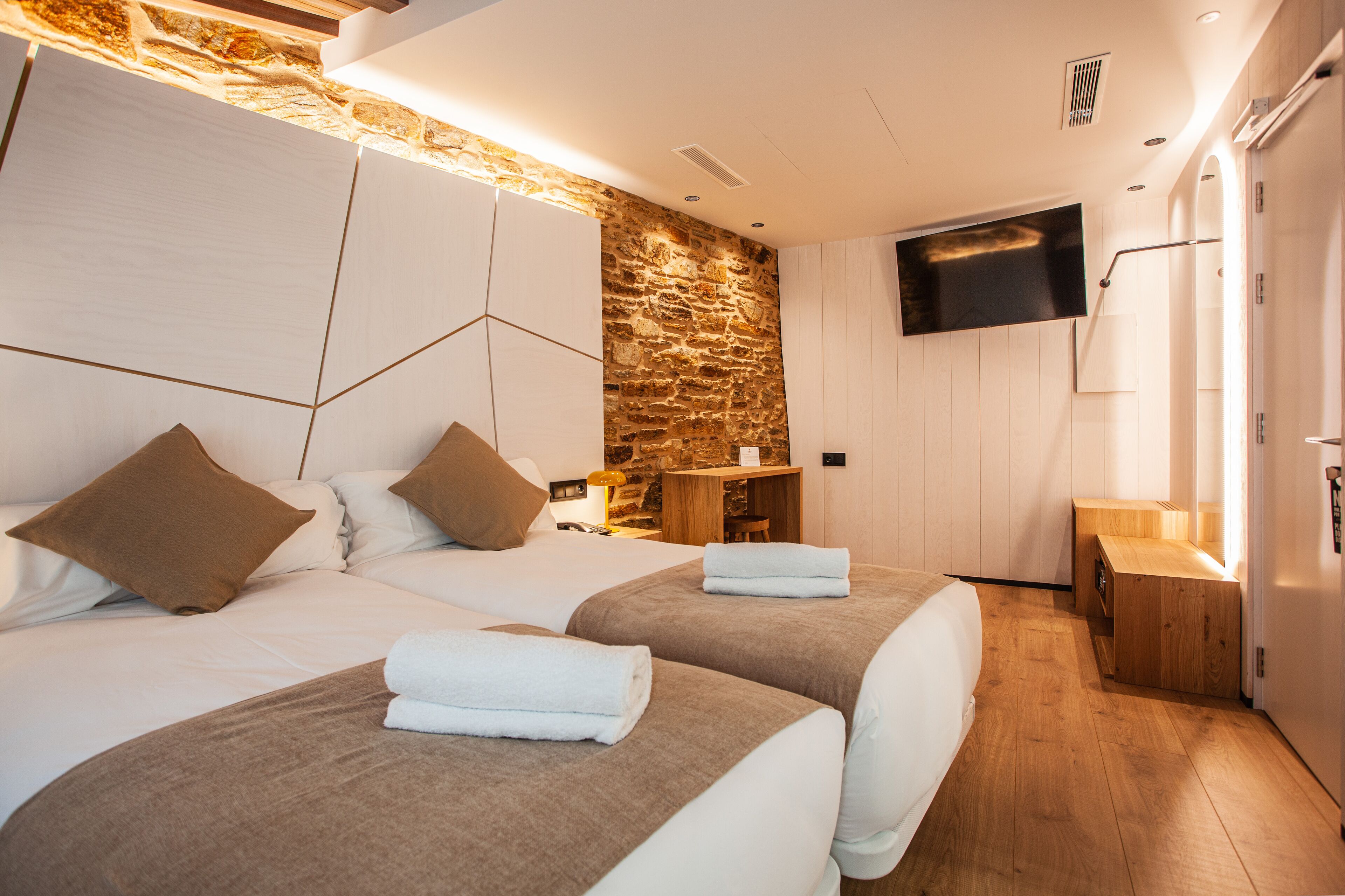 Habitación de hotel con dos camas, una pared de piedra, un televisor de pantalla plana y un armario de madera.