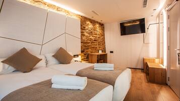 Habitación de hotel con dos camas, una pared de piedra, un televisor de pantalla plana y un armario de madera.