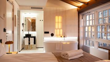 Una habitación de hotel moderna con una cama grande, una bañera y vistas a la ciudad a través de amplios ventanales.