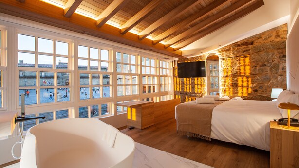 A bedroom with a large window, a bathtub, a bed, and a stone wall. -  Hotel Plaza Obradoiro by Bossh! Hotels (Santiago de Compostela)