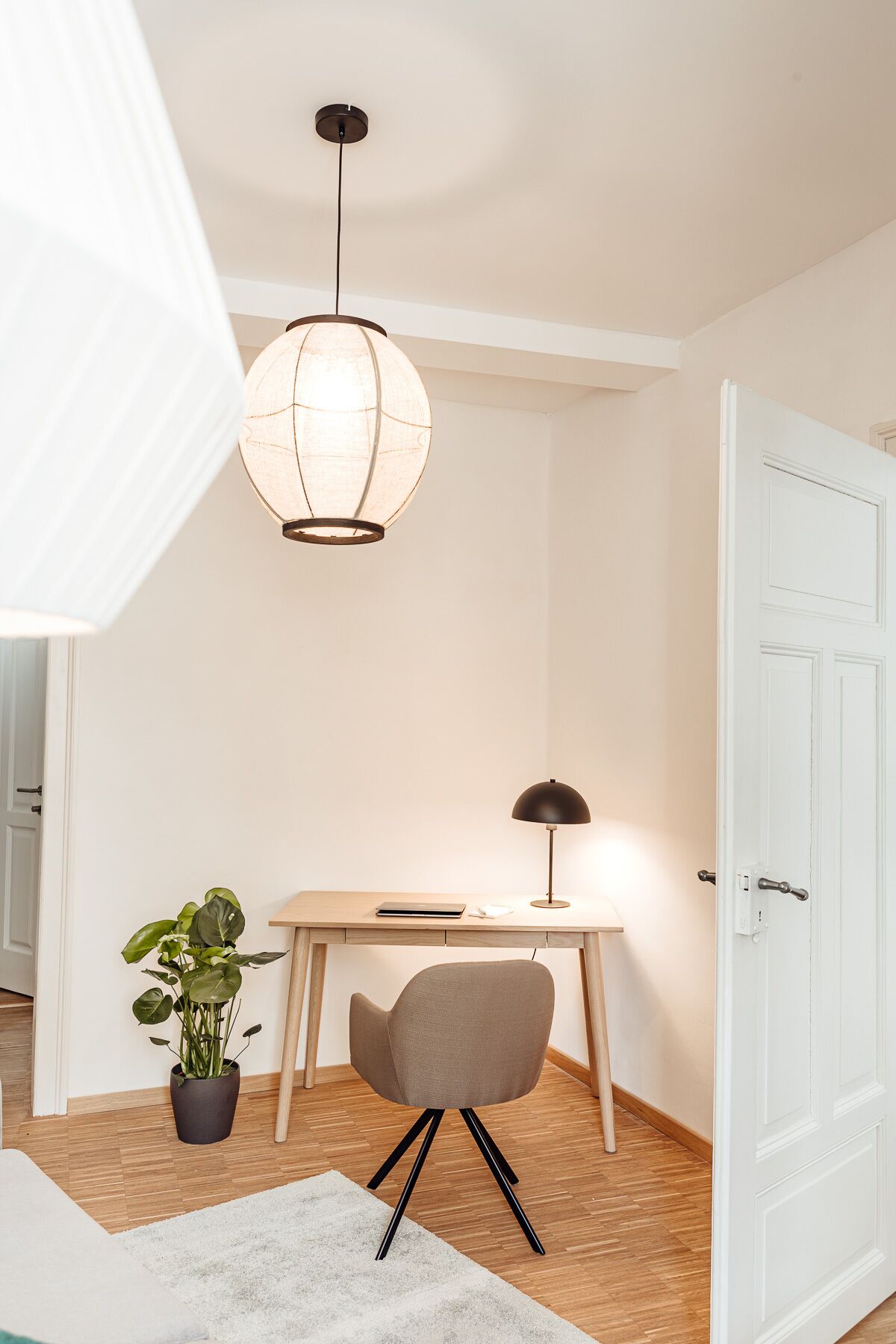 A room with a desk, chair, potted plant, and a hanging light fixture.