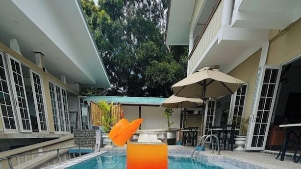 Un vaso de cóctel de naranja sobre una mesa, junto a una piscina con vista a un edificio y árboles al fondo.