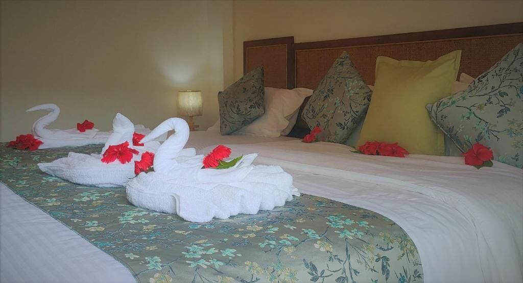 A hotel room with a bed featuring floral bedding, decorative swan pillows, and red flowers.