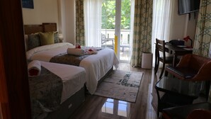 Una habitación de hotel con cama, escritorio, silla, televisor y balcón con cortinas.