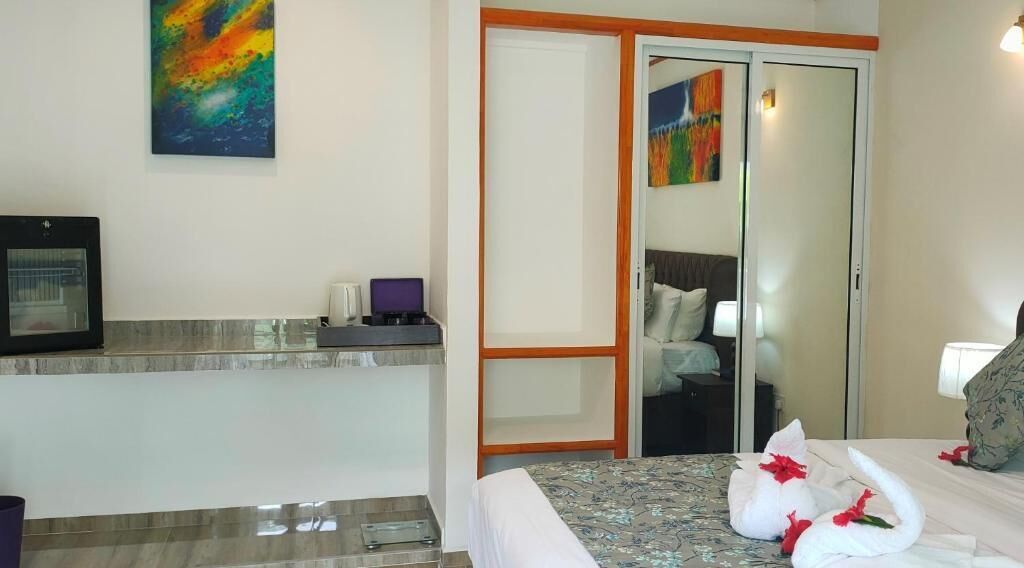 A hotel room with a bed, a desk with a computer, a mirror, and a painting on the wall.