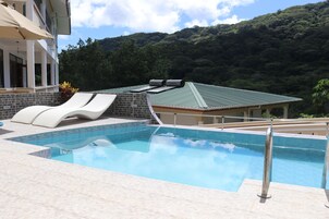 Una piscina con dos sillas reclinables y una terraza solárium, con montañas al fondo.