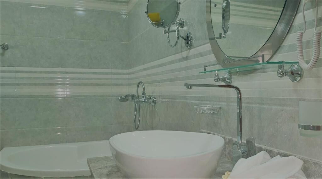 A bathroom with a freestanding bathtub, a glass-enclosed vanity, and a wall-mounted mirror.