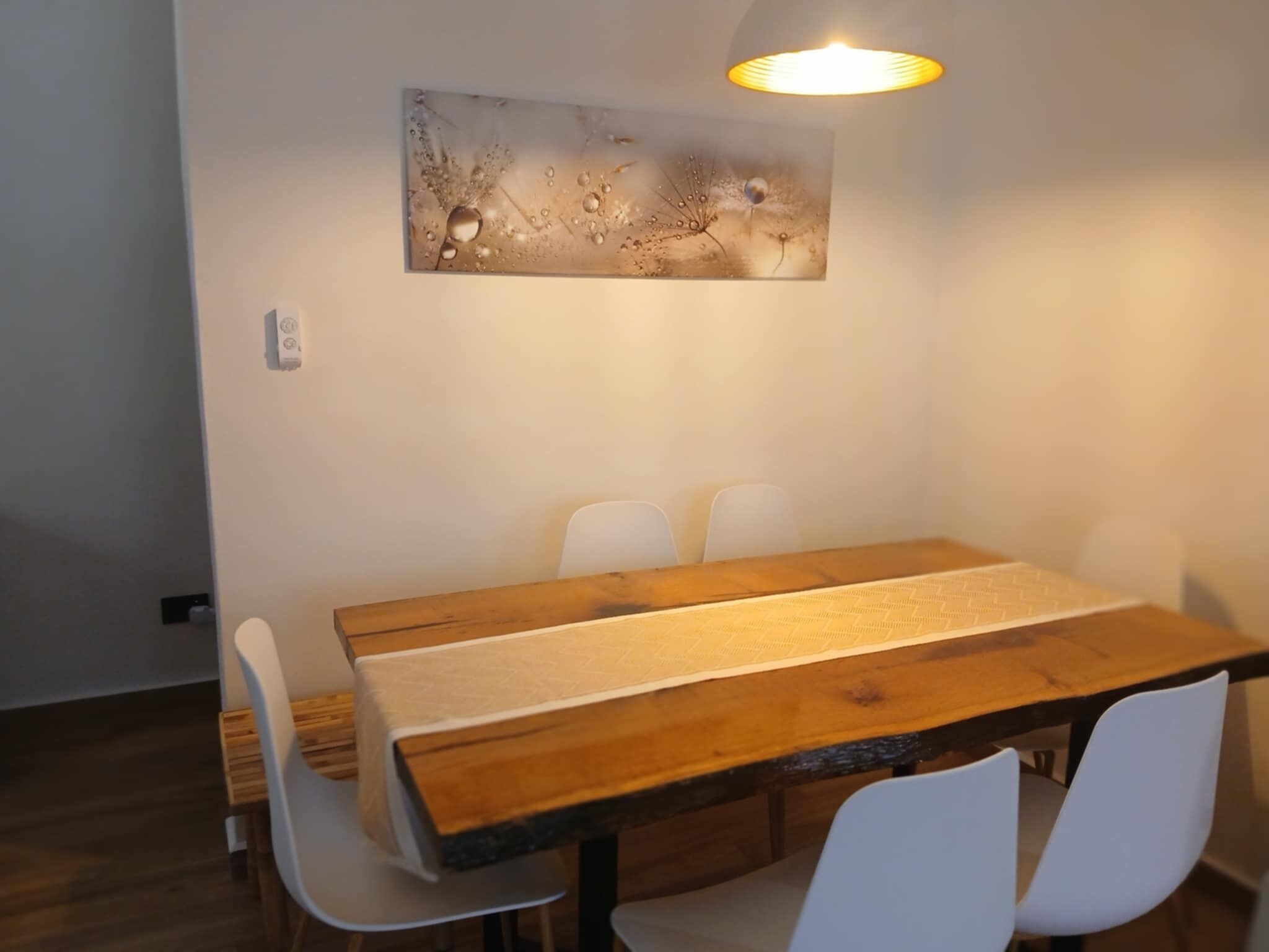 A dining area with a wooden table, white chairs, and a wall-mounted light fixture.