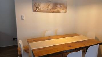 A dining area with a wooden table, white chairs, and a wall-mounted light fixture.