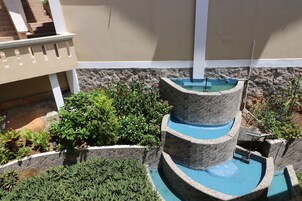 Una fuente escalonada con varios niveles, escalones de piedra y una alberca, rodeada de abundante vegetación y un muro de piedra.