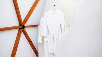 A room with a wooden ceiling structure, a white robe hanging on a hook, and a brown rug on the floor.