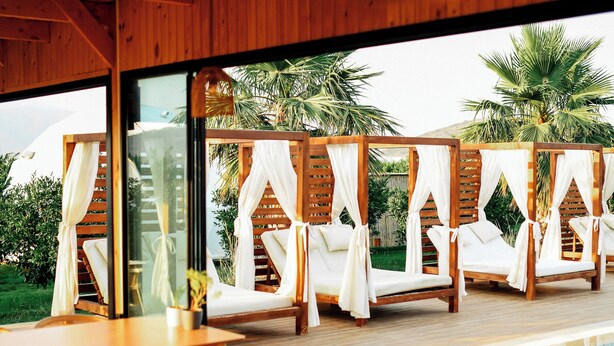 A modern pool area with wooden deck, lounge chairs, and a glass-enclosed space with curtains.