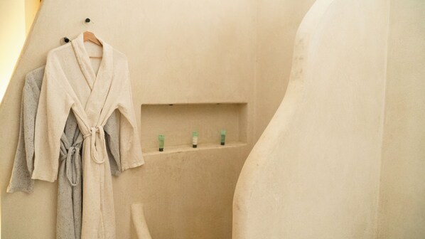 A bathroom with a beige wall, a towel rack with a robe, and a shelf with toiletries.