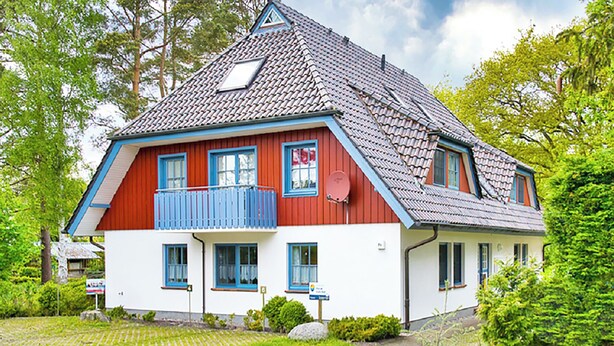 Ett tvåvåningshus med en röd och vit fasad, en blå balkong och ett sluttande tak.