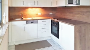 Ett kompakt kök med vita skåp, en inbyggd mikrovågsugn, en diskmaskin och en bänkskiva i trä.