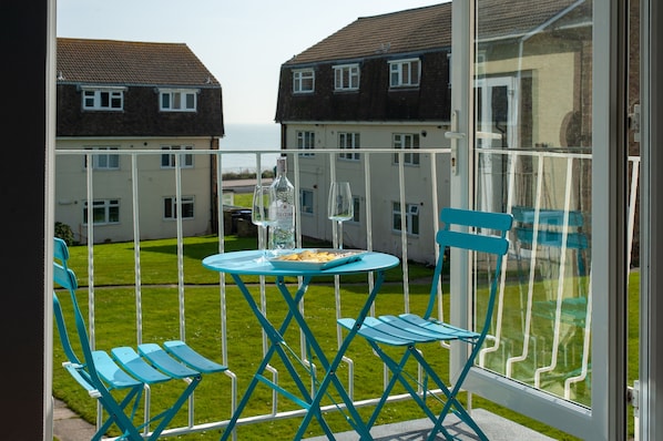 A balcony with a table and chairs, overlooking a grassy area and houses.