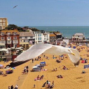 A beach with people, umbrellas, and buildings in the background.
