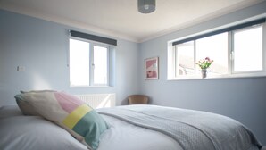 Ein Schlafzimmer mit einem Bett, zwei Fenstern, einem Heizkörper und einem Sessel.