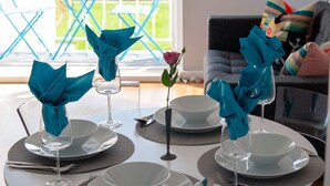 Ein Esstisch ist gedeckt mit weißen Tellern, Schüsseln und Weingläsern, jedes mit einer blauen Serviette.
