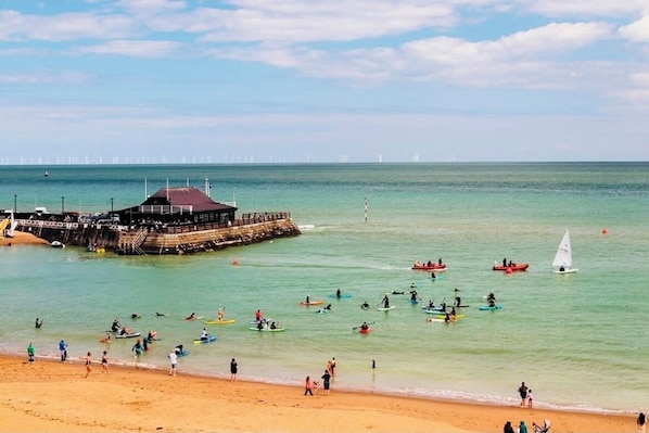 Une plage avec une jetée, une eau claire et des gens qui pratiquent des activités nautiques.